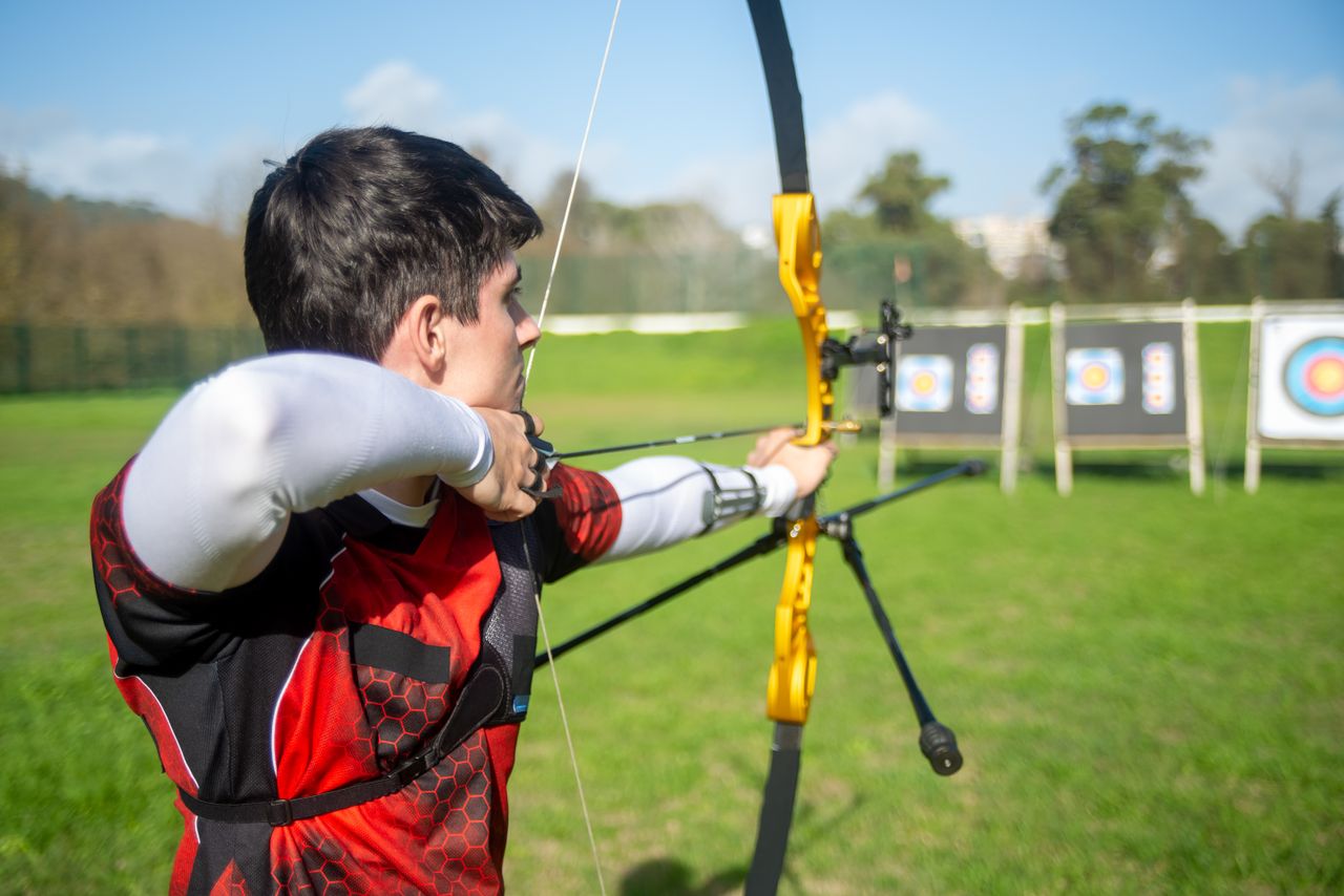 services-03 An archer aiming a bow at targets in an outdoor field on a sunny day.