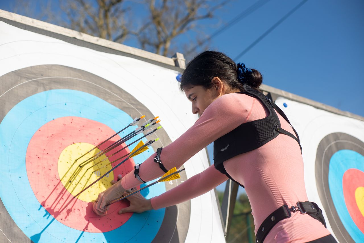 Crafting Captivating Headlines: Your awesome post title goes here A female archer adjusts arrows on a target during a sunny day, showcasing precise archery skills.